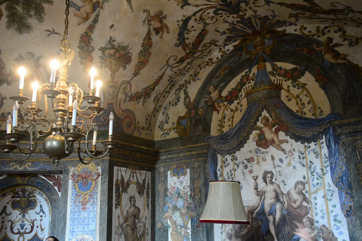 Fragment Sali Terrena z błękitnym baldachimem z draperią namalowanym na tle sceny mitologicznej, girlandami i puttami na sklepieniu oraz mosiężnym żyrandolem.